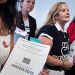 A group of women carry copies of the Epstein files in their hands while standing in a hallway.
