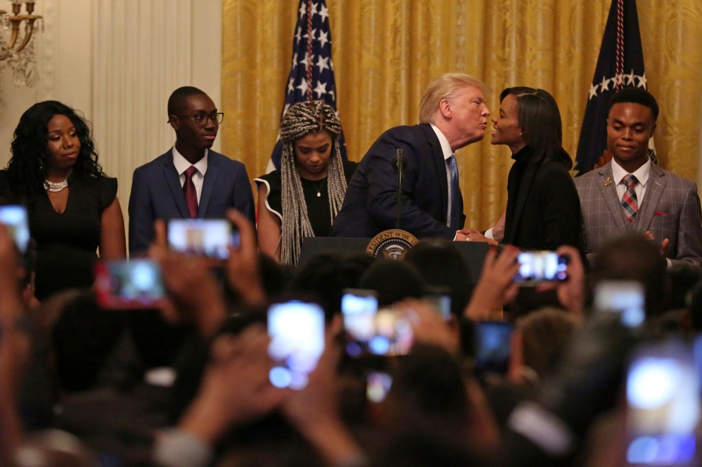 Trump leans over to kiss Owens while a crowd of people holding up phones watches alongside several others watching them onstage.