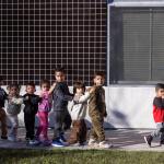 A line of young students hold hands walking outside of a school.