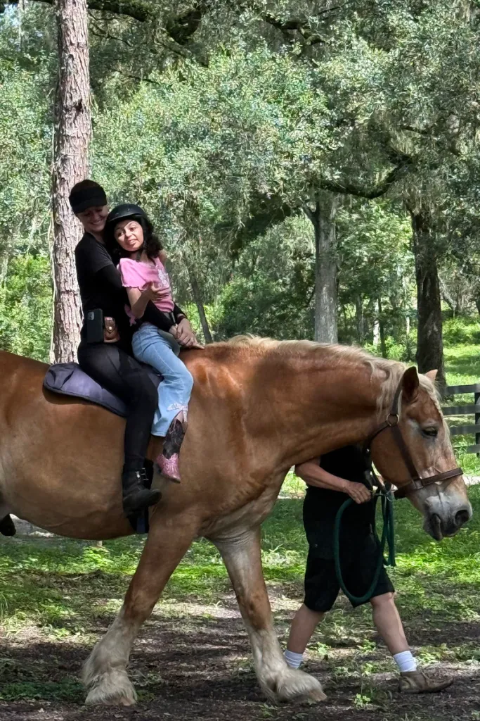 Lily on horseback being held up by a woman as another person walks the horse.