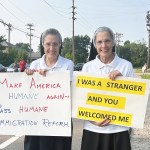 Two Catholic nuns hold signs related to immigration enforcement outside of an ICE facility.