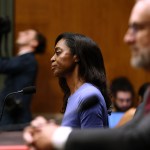 Schwartz sitting at a desk surrounded by white men in the foreground and background.