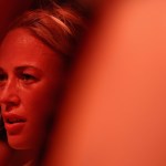 Sophie Cunningham is seen in close-up through a blurred foreground, her face lit in red-orange light.
