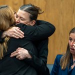 Two women hug while another person sits near them in a courtroom.