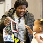 Edythe Smith smiles while holding up a soft activity book as her daughter Judith reaches toward it.