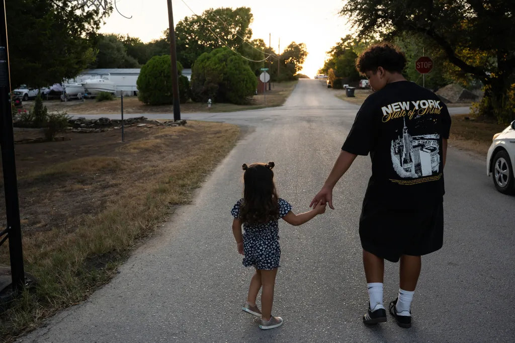 Mackenzie walks hand in hand with her brother, Luke, down a residential street at sunset.