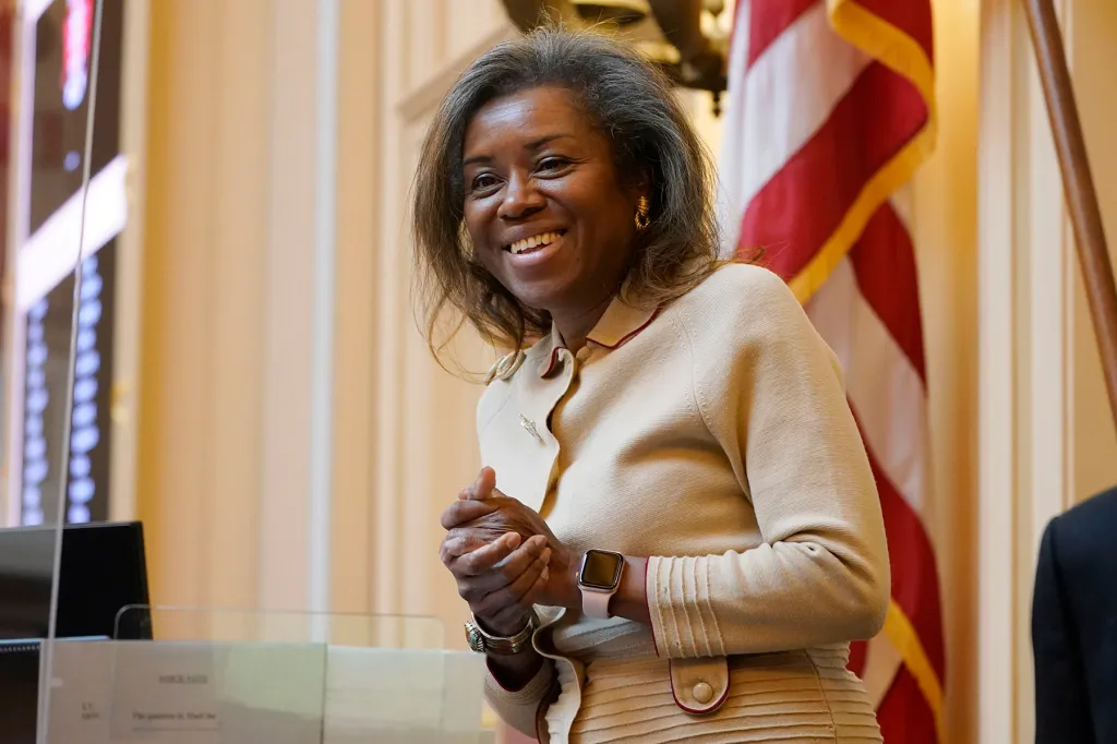Winsome Earle-Sears smiles while standing at a lectern, with an American flag behind her.