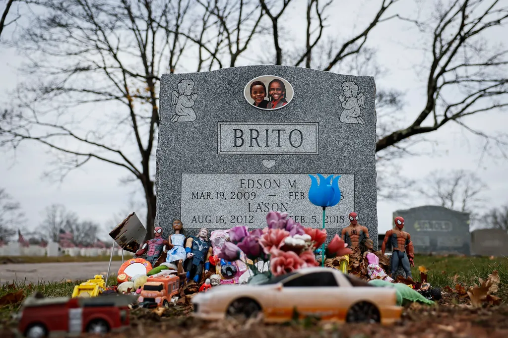 A gravestone for two children, Edson and Lason Brito, is surrounded by toys, flowers and superhero figurines, with a photo of the boys displayed near the top.