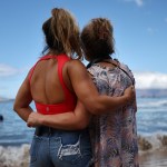 Two women embrace at the edge of the shore in Hawaii.