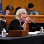 Gillibrand gesticulates with eyeglasses in hand from a chair in Congress.