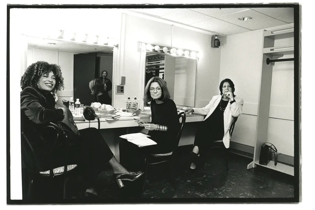 Three women sit in chairs in a dressing room turned toward the camera.