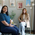 Two people sit in chairs looking at the camera.