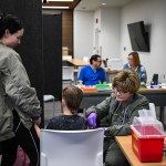 A nurse administers a vaccine to a child while others look on in the room.