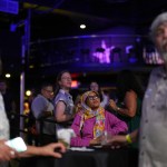 A woman looks up while seated at a table and surrounded by other attendees also looking up at something offscreen.