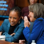 Alsobrooks and Blunt Rochester laugh as they whisper to each other while seated together.