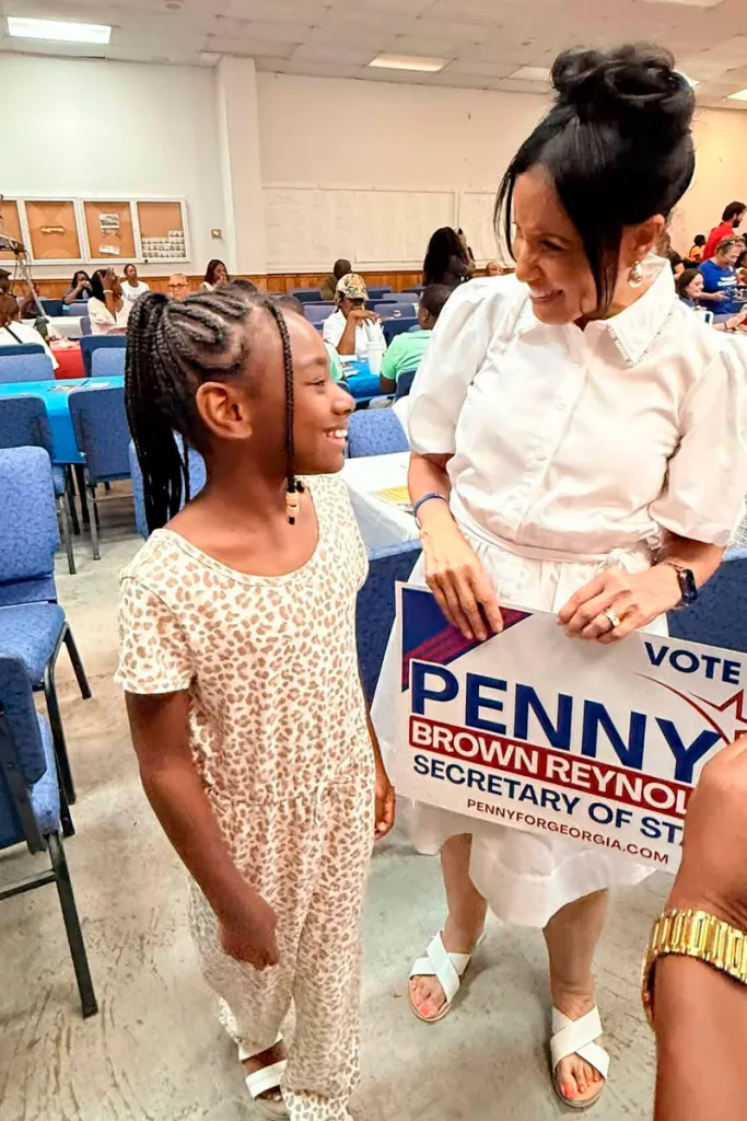 Judge Penny Brown Reynolds speaks to a young girl at a campaign event while holding a campaign sign. Black women in politics