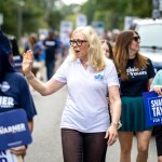 Taylor walks down the street waving while surrounded by people holding campaign signs.
