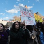 A group of students gather and carry signs in protest.
