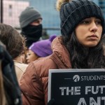 A woman wearing a black knit hat and brown puffer jacket holds a Students for Life anti-abortion sign at a rally.