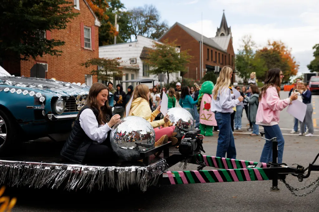 A woman rides a float with a disco ball at the helm as many people walk alongside.